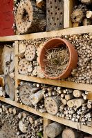 Insect house made from logs, bamboos and straw in clay pot