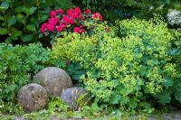 Three stone balls next to Alchemilla mollis and Impatiens