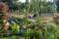 Garden designer Wolfgang Seebauer has planted perennials combined with Roses and Vegetables in a traditional rural style containing Rosa 'Ghislaine de Féligonde' - Rambler, Achillea ptarmica, Campanula lactiflora, Campanula punctata, Clematis viticella 'Etoile Violette', Clematis viticella 'Kaaru', Erigeron 'Mrs. Beale', Tanacetum parthenium and Tradescantia. In the background there is a pigeon house in a meadow with trees and grazing cows.'