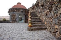 Lava stone steps, edged with clay pots planted with Cacti variety, including Ferocactus - El Jardin de Cactus, Lanzarote, Canary Islands.  