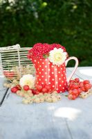 Red and white currants with polka dot jug and flowers on wooden table

