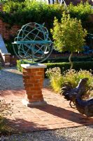Metal armillary sundial and hen statue on red brick patio, Oxfordshire
