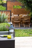 Small town garden with wooden table and chairs, lantern, screens made of mild steel, decking and raised bed 