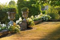 View from terrace with white climbing Rosa and ornate stone urns 
