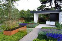 Cor-Ten steel water trough surrounded by Agapanthus, Stipa tenuissima and Lavandula, next to a black and white pavilion with white chairs - 'Vestra Wealth's Gray's Garden', Gold Medal Winner, RHS Hampton Court Flower Show 2011