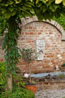 Wall mounted head of Neptune water spout above brick pool, Garden Hackl, Mistelbach Austria