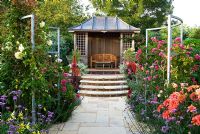 Central pond and summerhouse feature in the sunken garden, constructed in 2005, surrounded by a colourful mass of perennials and annuals including Verbena bonariensis, Dahlias, Rosa, Cleomes and scarlet Lobelia cardinalis - Isle of Wight, UK