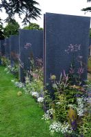 Herbaceous perennial planting between repeating vertical panels of recycled plastic with granite-like effect