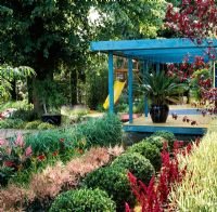 Painted pergola over decking with box balls and Astilbes in the foreground. Children's slide in background - RHS Hampton Court Flower Show 1998