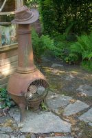 Chiminea by shed and stone path in shaded part of garden