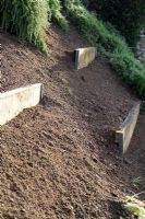 Method of stabilising and terracing a steep bank by embedding thick pieces of treated timber secured with metal angle.