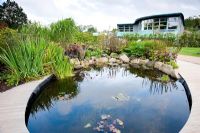 Bramall Learning Centre and Library seen from the pond in the Teaching Garden -  RHS Garden Harlow Carr, Harrogate, North Yorkshire, UK