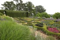 The Broughton Grange Box parterre - the design is based on the structure of leaves viewed under a microscope infilled with blocks of colour through the year with different plants depending on the season. Buxus parterre with Verbena x hybrida, Cosmos, Antirrhinum and Kale with a Hornbeam hedge in the background