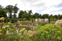 Thalictrum, Helenium 'Moerheim Beauty', Geranium 'Patricia', Euphorbia cornigera and Aruncus dioicus in the foreground.  Large pond, patio and large greenhouse in distance, surrounded by fastigiate Taxus baccata - Broughton Grange