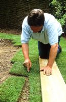 Making a lawn from turf. Trimming with a knife whilst kneeling on a wooden board to protect grass