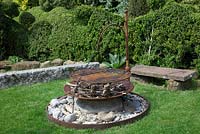 Rusty firepit sitting on a large stone boulder, with fir cones and kindling