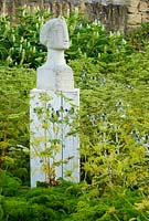 Portland stone head carved by local artist Tom Clark, amongst a mass of self seeded Eryngium x giganteum, ferny Ligusticum lucidum against a backdrop of white Phytolacca americana - Yews Farm, Martock, Somerset, UK