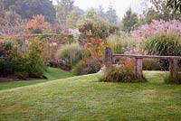 Landscaped hillock with decorative seat overlooking autumn borders - Marchants Hardy Plants Nursery, Sussex