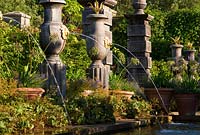 Rill pool flanked by turned oak urns spouting water through gilded lions' heads, with golden agaves in their tops. The Collector Earl's Garden designed by Julian and Isabel Bannerman. 
