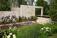 A garden inspired by the Arts And Crafts Movement. Formal paths and terraces combine with a water channel. Monolithic stone walls and an oak bench that appears to float. Focal point is an energy wave sculpture made from copper rings. Planting style is woodland edge with buxus domes - The M & G Garden