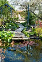 Pond with metal sculpture,decking and path with Narcissus poeticus