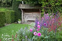 Covered seating area in country garden with perennial border including, Dahlia, Persicaria amplexicaulis, Lobelia vedrariensis, Lythrum salicaria 