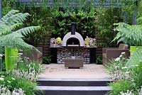 Outdoor living cooking area with wood burning oven and back wall planted with ferns and bamboo. Live Outdoors. Hampton Court Palace flower show 2012.