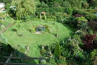 Overview of garden with hexagonal shaped lawn and central pond with millstone fountain