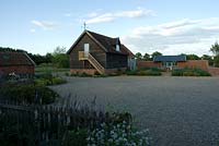 View form house across picket fence to converted barn with cockerel weather and the Mediterranean Garden. June