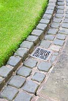 Cobble setts neatly surrounding drain and edging lawn and stone slab path