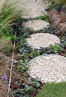 Path of circular containers filled with gravel, bark chippings and Viola with edging by ornamental grasses in the 'One Man Went To Mow' garden,  RHS Tatton Flower Show 2012