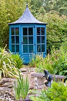 Frog fontain and stone bench in pond area, planting includes Kniphofia 'Dorset Sentry', Osmundo regalis, Phylostachys nigra and Phormium 'Yellow Wave'