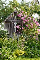 Bavarian wayside cross with climbing roses and perennials in a country garden