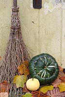 Besom broom and squashes on doorstep with fallen autumn leaves from Liriodendron tulipifera