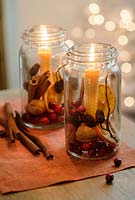 Old glass jars filled with cranberries, cinnamon sticks, dried orange slices, walnuts and larch cones with beeswax candles