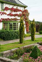 Arts and Crafts house deisgned by Charles Voysey, 1895, with flaming reds of Vitis cognetiae and a pair of fastigiate golden yew - Perrycroft, Upper Colwall, Herefordshire, UK