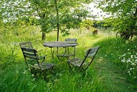 Vintage folding garden table and chairs beside grass path in wild garden with oxeye daisies and cherry trees - The Mill House, Little Sampford, Essex