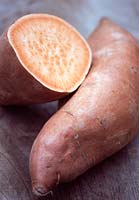 Ipomoea batatas - One whole and one half of a sweet potato on a rustic wooden surface