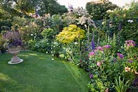 Border around circular lawn includes Lilium 'Zulu', Rosa 'Rhapsody in Blue', Delphinium 'Black Knight', Rosa 'Maigold', Pyracantha, Choisya 'Tenata Sundance', Hosta 'Great Expectations', Stipa gigantea and Euphorbia wulfenii