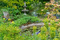 Large pond surrounded with densely planted perennials and container plants