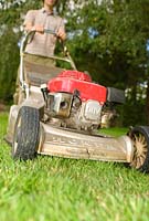 Man cutting lawn with petrol driven rotary lawnmower