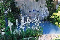 Metal chairs and table. Campanula and lupins in white border, Willow Pattern garden, Hampton Court Flower show 2013, Design -  Sue Thomas