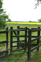 Garden rail fencing with traditional 'kissing gate' opening on to a field of Oilseed Rape and open countryside beyond - Open Gardens Day 2013, Bardwell, Suffolk