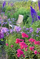 Wooden bench in border planted with Phlox paniculata 'Lilac Time', Phlox paniculata 'Grenadine Dream', Rosa and Delphinium 'Pagan Purples'