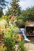 Woman relaxing, drinking tea in small suburban garden