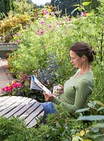 Woman reading newspaper and drinking tea in small suburban garden