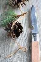 Step by step of making a simple, rustic Christmas garland with fir cones and pine needles - Tie another simple knot two inches from the end, leaving a small loop for a drawing pin or nail to go through. Cut off any excess twine