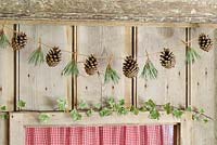 Step by step of making a simple, rustic Christmas garland with fir cones and pine needles - The finished garland hanging on a wooden door