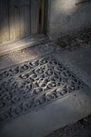 Cast iron filligree door mat by old wooden door.