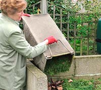 Woman adding grass clippings from rotary mower to the compost heap 